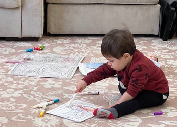 Child focused on coloring with markers surrounded by drawings and crayons on the floor