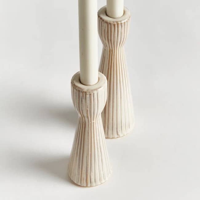 Two ribbed ceramic candle holders, each holding a long white candle, displayed on a plain background