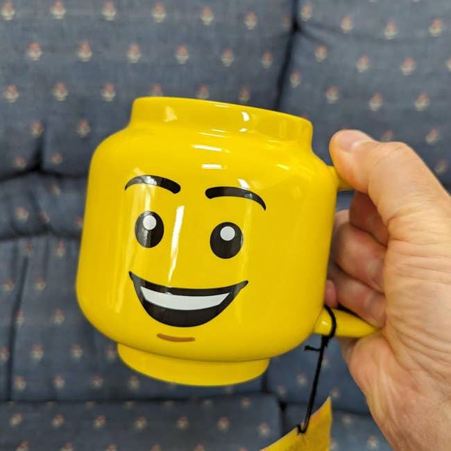 Person holding a mug shaped similar  a smiling face, designed to lucifer   a artifact  head, with a salient  handle