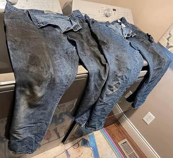 reviewer photo of two pairs of dirty jeans on top of a washing machine