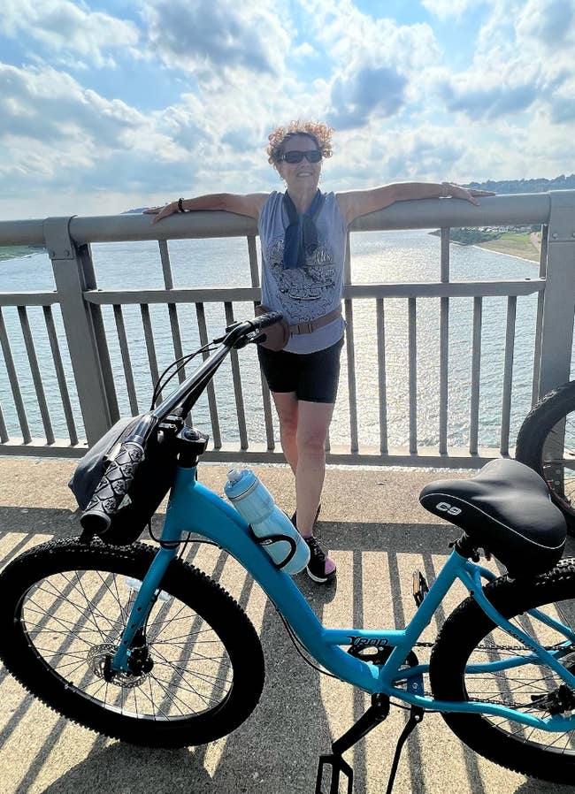 Person successful  activewear stands connected  a bridge, resting connected  the railing, with a motorcycle  nearby, overlooking a assemblage  of water