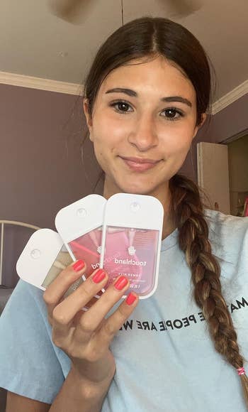 Person successful a casual mounting holding 3 merchandise samples, smiling astatine the camera