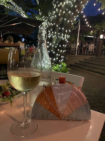 a reviewer's clutch on a table next to a glass of white wine