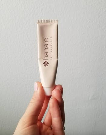 Reviewer holding up beige lip treatment tube 