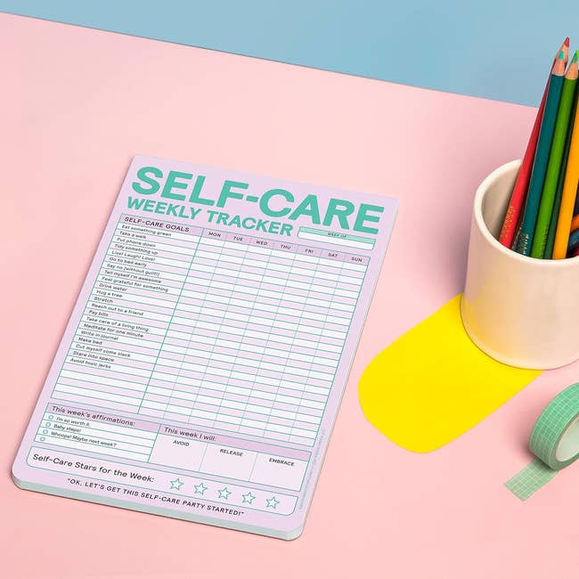 Self-care play   tracker pad with structured extremity   sections beside a cupful  of colored pencils, acceptable   connected  a desk