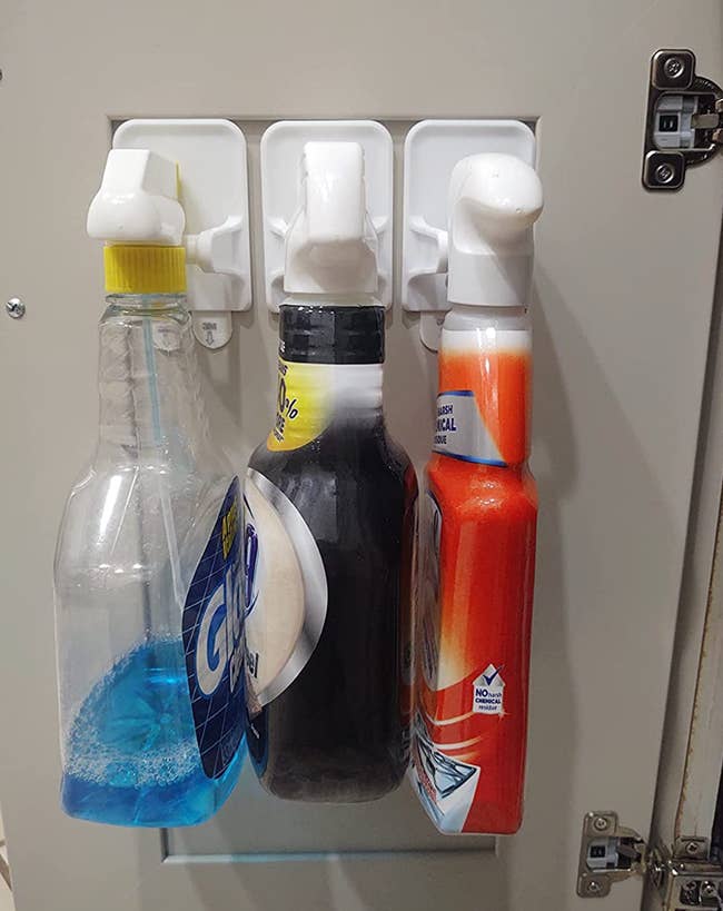 Three bottles hung on white Command hooks to the inside of a cabinet 