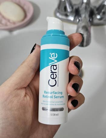 Person holding a bottle of CeraVe Resurfacing Retinol Serum over a sink