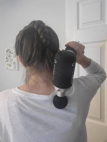 reviewer using black massage gun to help relieve muscle tension on their shoulder