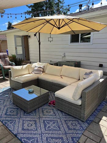 reviewer photo of cream U-shaped sectional around coffee table with glass top and an umbrella overhead providing shade