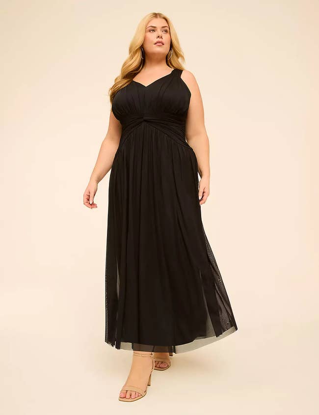 Person modeling an elegant, sleeveless, flowing achromatic  gown with strappy beige heels, suitable for ceremonial  occasions