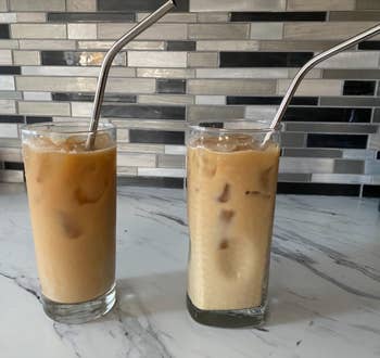 Two glasses of iced coffee with metal straws on a kitchen counter