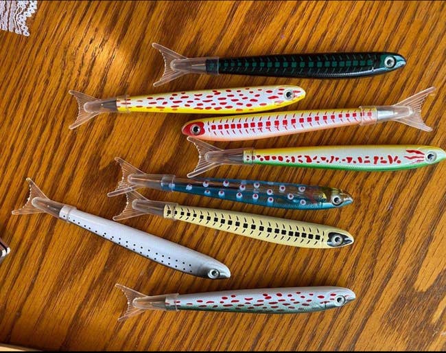 Nine fishing lures with various patterns and designs laid out on a wooden surface