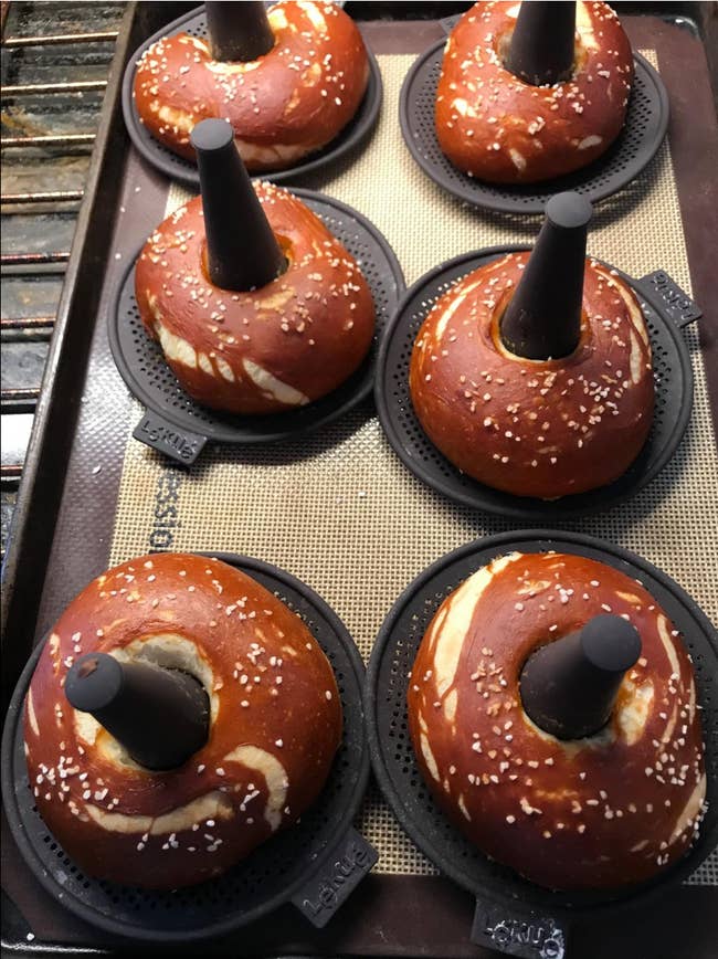 black silicone mats with cones emerging from them to create holes in six cooked pretzel bagels 