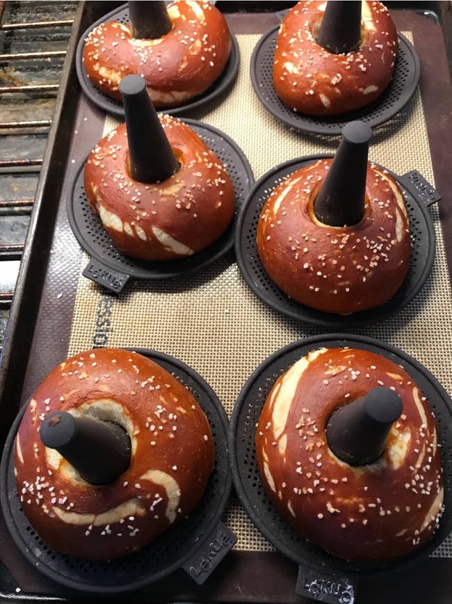 black silicone mats with cones emerging from them to create holes in six cooked pretzel bagels 