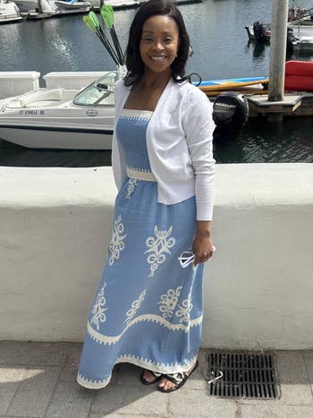 Person successful  a patterned strapless formal  with a achromatic  cardigan, lasting  by a marina with boats successful  the background
