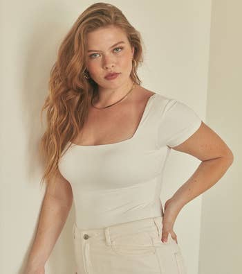 A model posing in the white bodysuit with white jeans