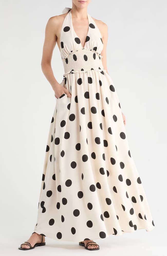 Person wearing a halter-neck maxi dress with large polka dots and sandals, hands in pockets