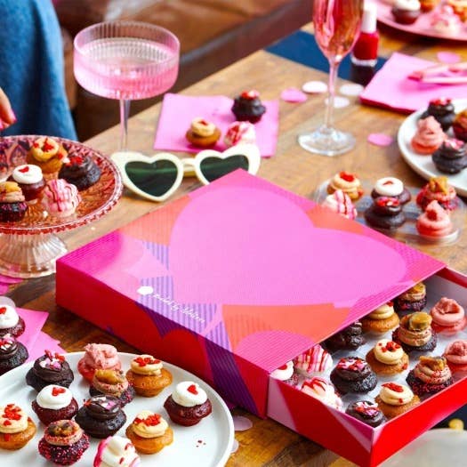 a box of mini cupcakes with plates of mini cupcakes around it