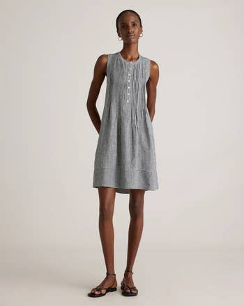 Model wearing a sleeveless checkered formal  with a buttoned front, styled simply   with hoop earrings and strappy sandals
