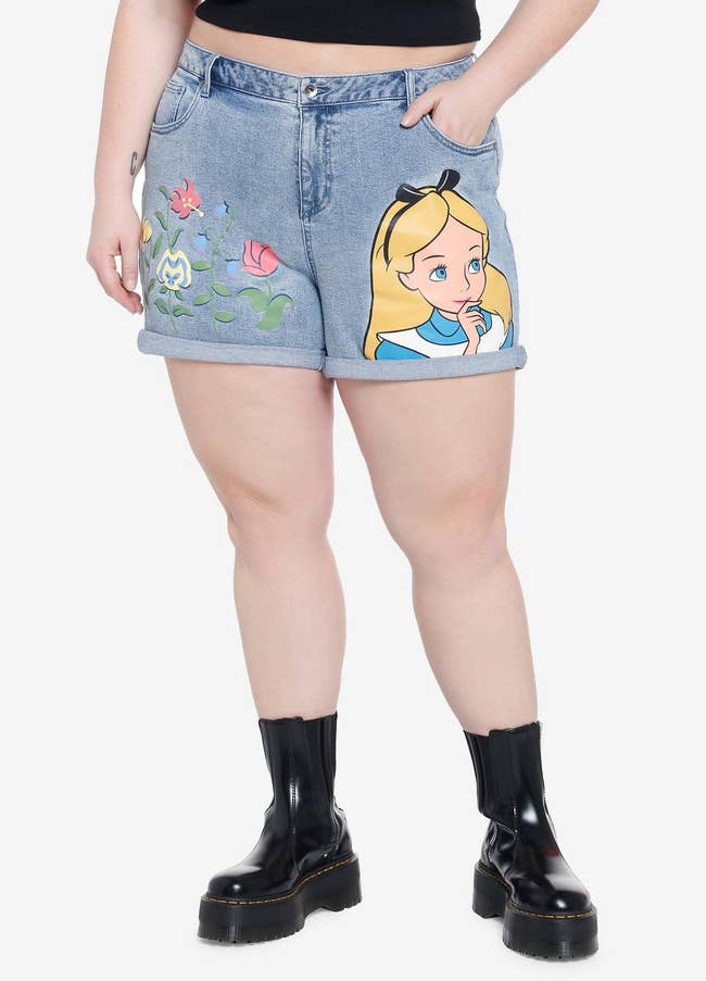 model in medium wash shorts with floral graphic on one side and alice on the other