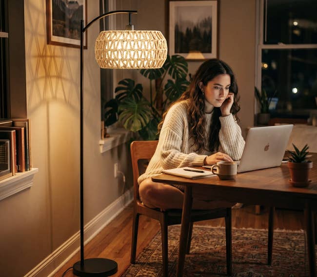 Person successful a cozy country utilizing a laptop astatine a woody table, with a lukewarm airy from an overhead lamp illuminating the scene