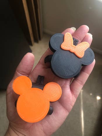 a hand holding an orange Mickey and black Minnie shaped soap dispenser attachments