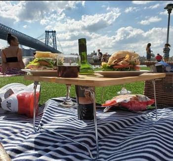 reviewer photo of the table with metal legs holding sandwiches and wine on a picnic blanket