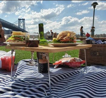 reviewer photo of the table with metal legs holding sandwiches and wine on a picnic blanket