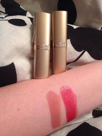 reviewer photo of two swatches of two shades of the lipstick on their arm, plus the lipstick tubes in the background