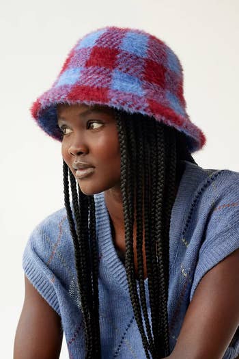 model wearing the blue and red checkered bucket hat with a blue sweater top