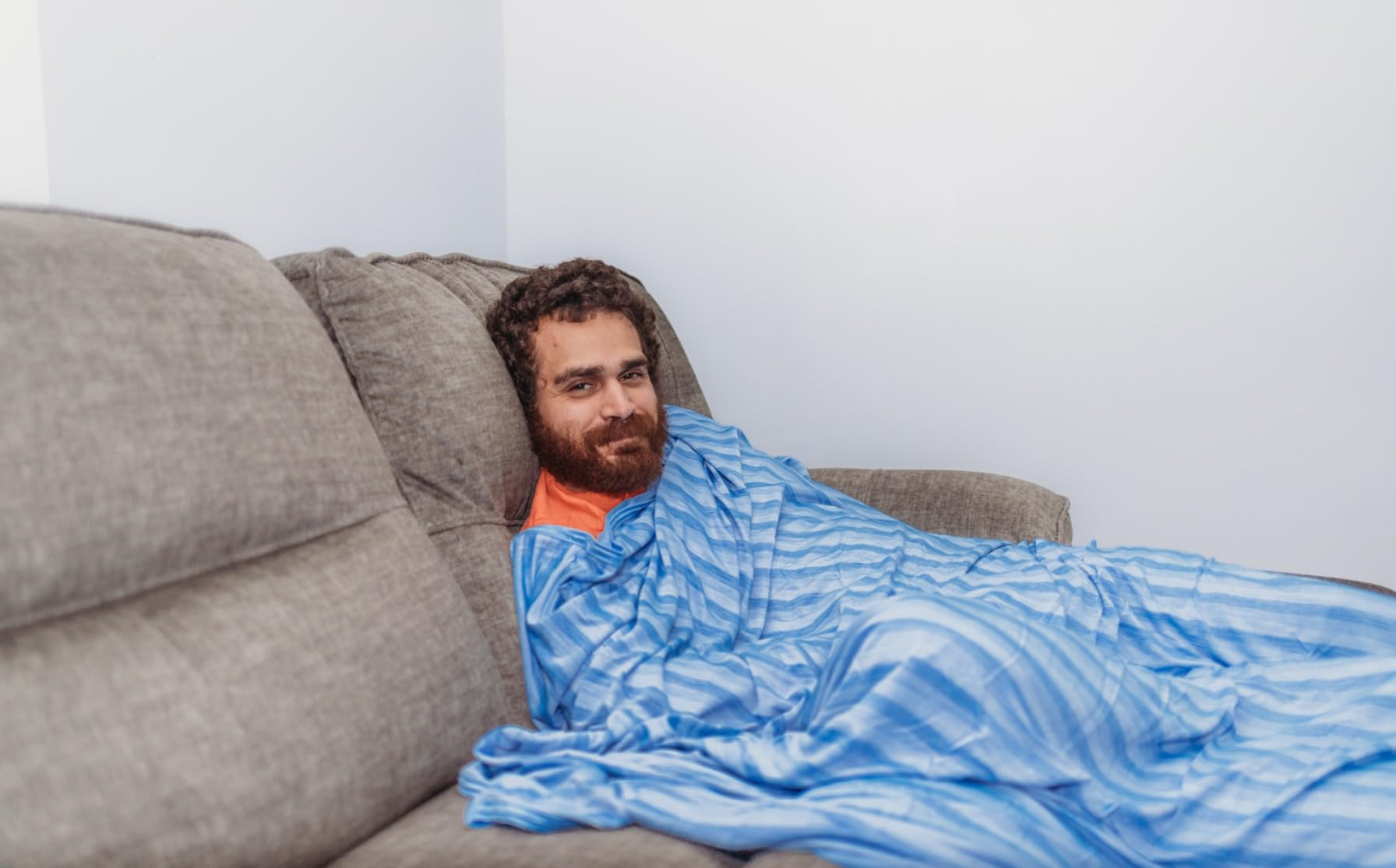 Person relaxing connected  a couch, wrapped successful  a striped blanket, looking towards the camera