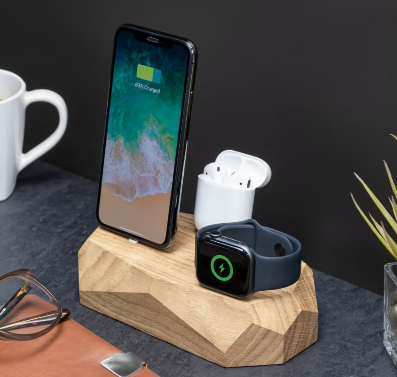 the charger with a light brown wood base and a phone, watch, and headphones charging in it