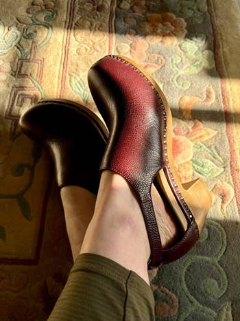 Feet shown wearing stylish clogs with a textured decorativeness and woody heels, resting connected a patterned carpet