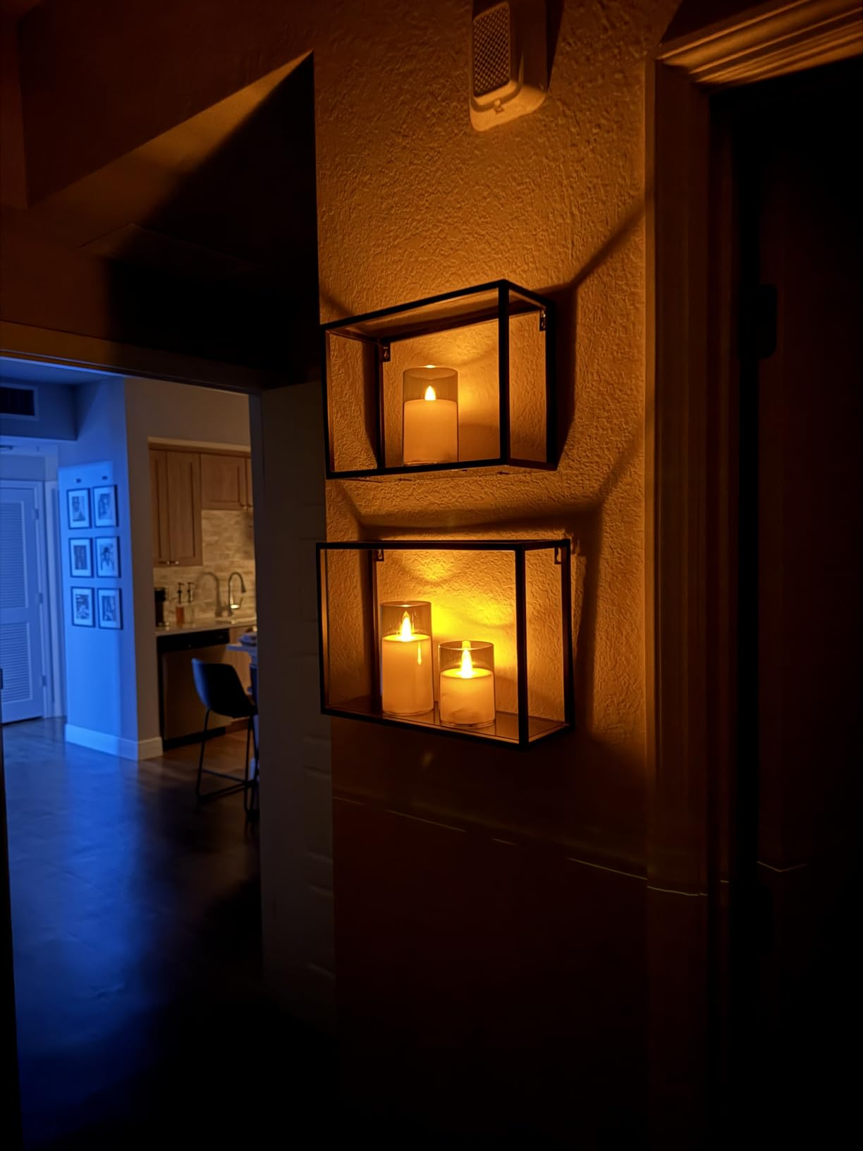 Two wall-mounted candle holders with lit candles make  a cozy ambiance successful  a dimly lit interior hallway, starring  to a disposable   room  area