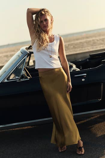 Person wearing a sleeveless apical and agelong skirt, lasting by a convertible car connected a beach. Style is casual and relaxed