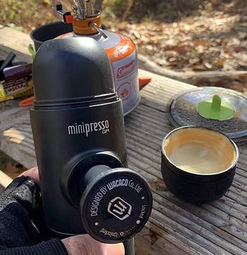 reviewer holding the black portable espresso maker at a campsite