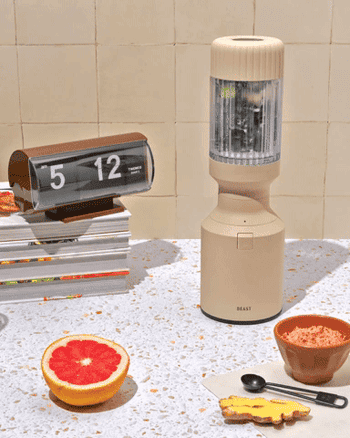 Portable blender on a table with sliced grapefruit, books, and a clock, suggesting a lifestyle setting