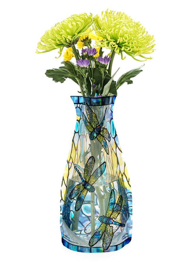 Blue and yellow glass tile inspired vase with dragonflies decorating it and green and purple flowers inside on a white background