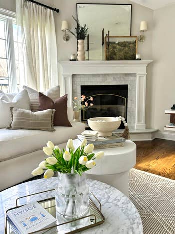 Stylish surviving country with achromatic sofa, accent pillows, and tulips connected a marble table. Books and decor items are arranged connected a circular broadside table