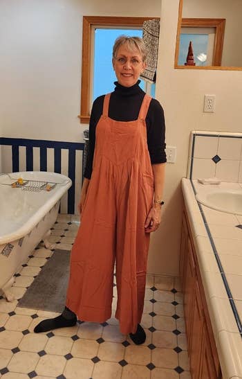 reviewer posing in the jumpsuit in orange over a black long sleeve top