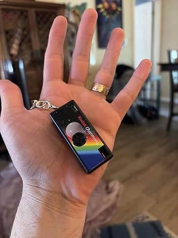 Hand holding a Kodak Mini Shot keychain camera with a rainbow stripe, highlighting retro design for a nostalgic shopping appeal