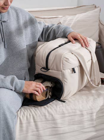 model zipping up a cream-colored backpack with shoes inside, demonstrating packing functionality