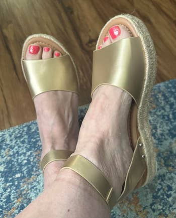 Person wearing golden open-toe sandals with ankle straps connected a textured bluish and woody floor