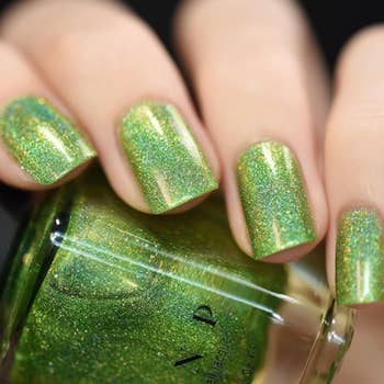 Entertainmment news Close-up shot of a hand with shiny, glitter-covered green nails, holding a bottle of matching nail polish