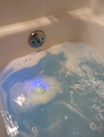 A bath fizz turning the water blue with the fizz and with the blue light inside it 