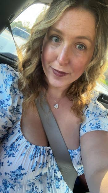Person successful  a floral blouse, seated successful  a car, wearing a necklace. They person  wavy hairsbreadth  and are looking astatine  the camera
