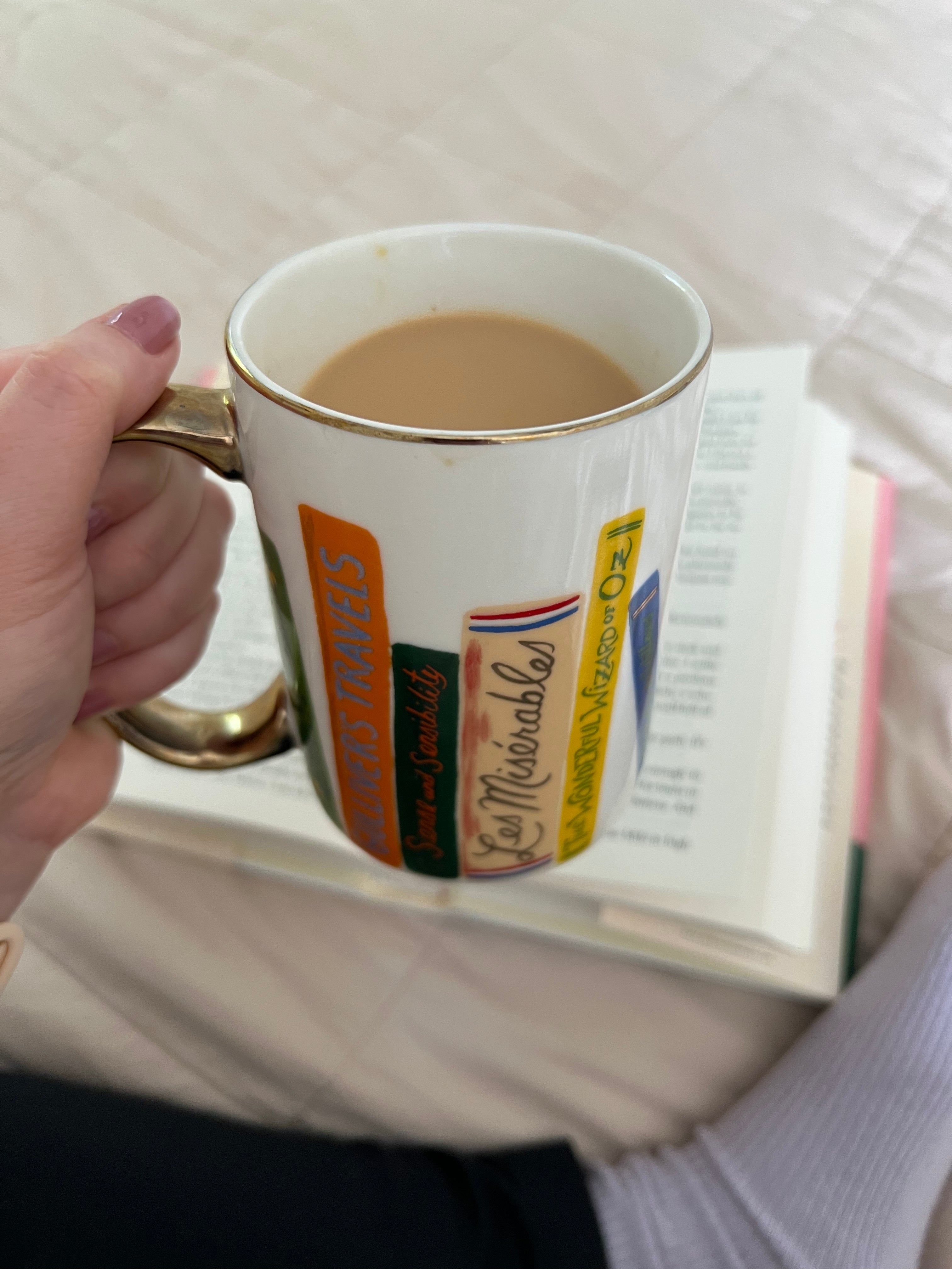 a mug with a gold handle and a design of books all around it