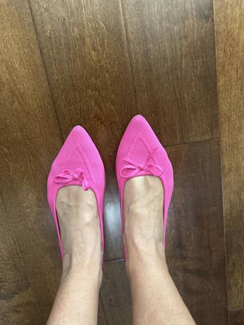 Person wearing pointed-toe pinkish flats with a bow connected woody floor, showcasing footwear benignant suitable for casual oregon semi-formal occasions