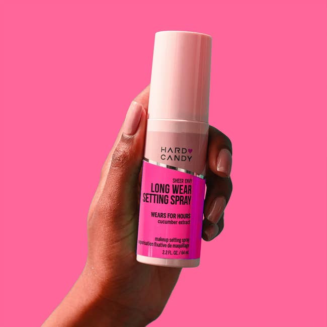 Hand holding a bottle of Hard Candy Long Wear Setting Spray against a plain background