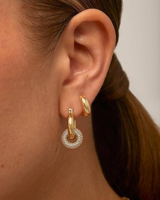 Close-up of a woman's ear wearing two earrings: a small gold hoop and a larger hoop with a gold and textured silver design